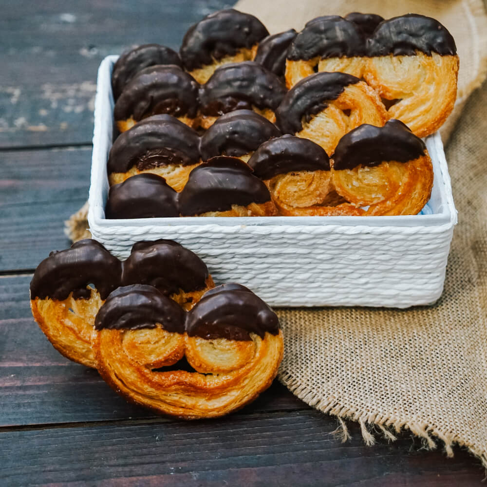 knusprige Schweinsohren mit Schokolade verziert in einer weißen Schale