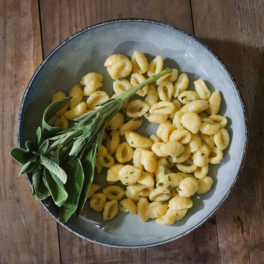 Ein Teller mit frisch gekochten, selbstgemachten Gnocchis auf einem Holztisch.