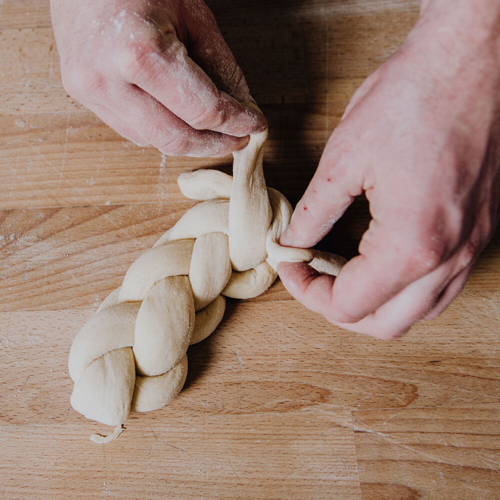 Hefeteig wird auf einer Holzarbeitsplatte geflochten