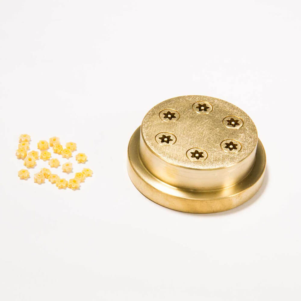 Matrize Nr. 325 - Stelline / Sterne Nudelmatrize Nr. 325 für Stern-Nudeln neben einigen Stern-Nudeln vor einem weißen Hintergrund.