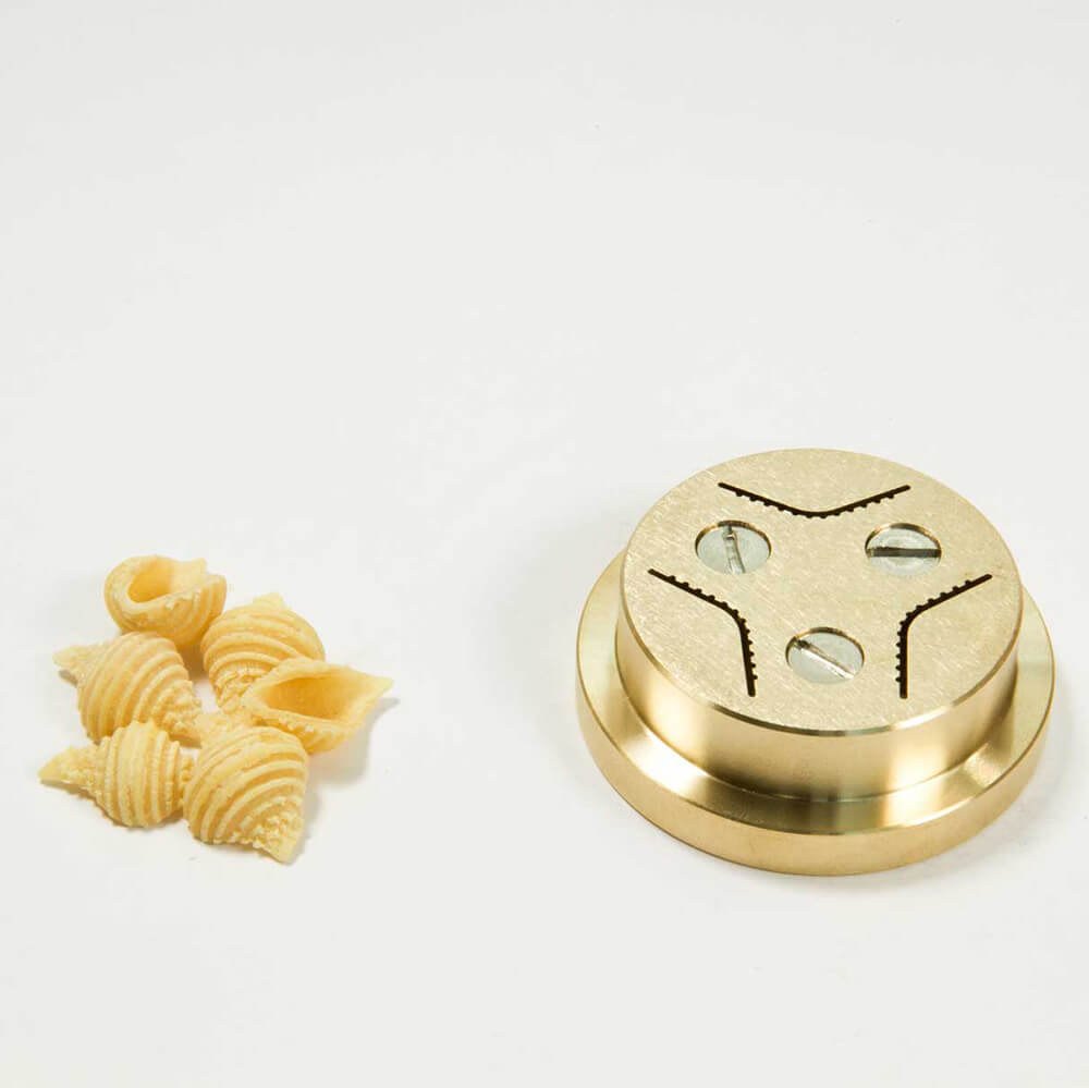 Matrize Nr. 50a - Conchiglie / Muscheln Nudelmatrize Nr. 50a für Conchiglie / Muschel-Nudeln neben einigen Muschel-Nudeln vor einem weißen Hintergrund.