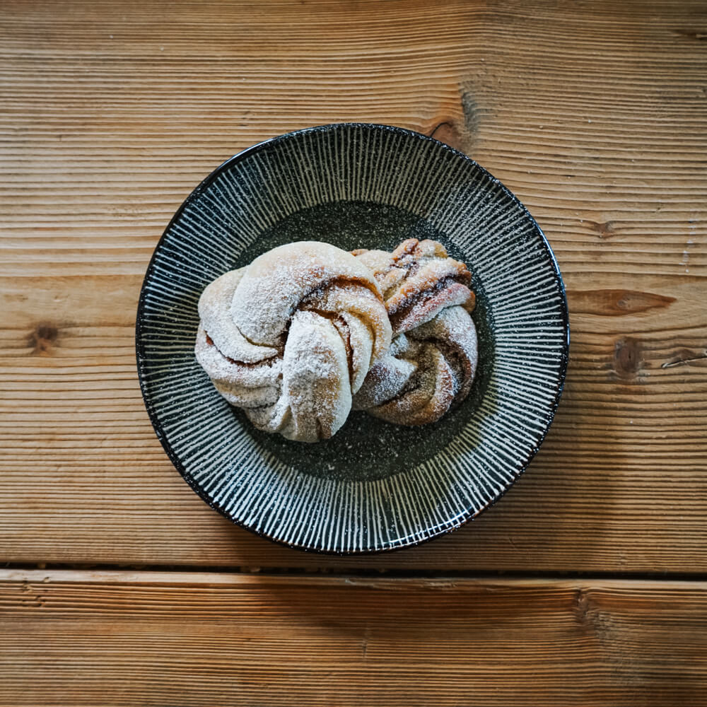 Rezept für Zimtknoten glutenfrei Zimtknoten mit Puderzucker bestreut auf einem schwarz-weiß gestreiften Teller