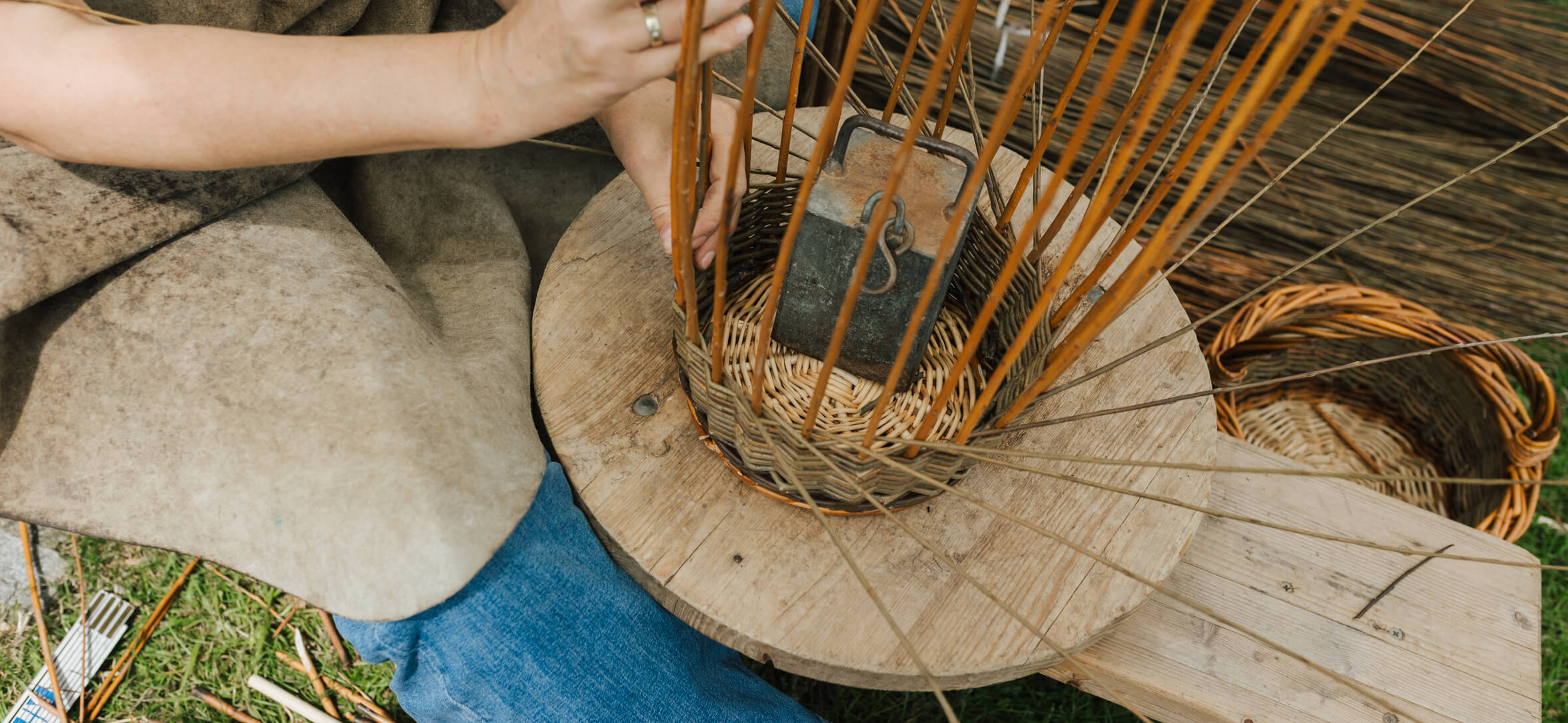 Korbflechterin beim Brotfest Korbflechterin arbeitet am einem Weidenkorb, umgeben von Naturmaterialien und trasditioneller Handwerksatmosphäre.