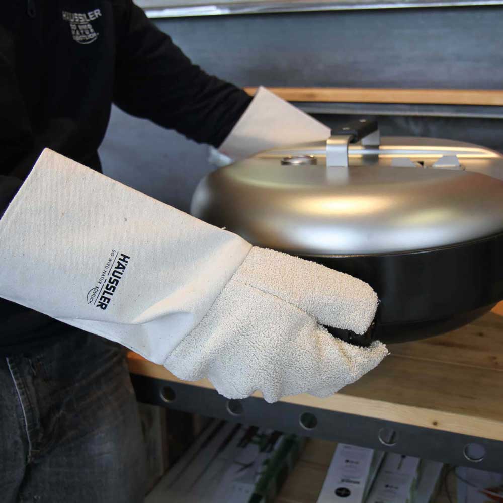 Backhandschuhe aus Frottee Weise Backhandschuhe aus Frottee mit einem Häussler Logo. Mit den Handschuhen wird eine Grillplatte gehalten.