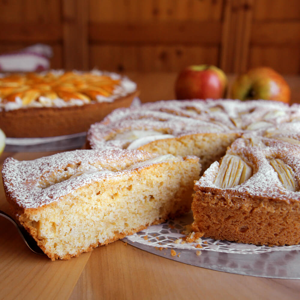 Rezept für Dinkelrührkuchen runder Dinkelrührkuchen mit Äpfeln und Puderzucker bestreut auf einer Kuchenplatte serviert