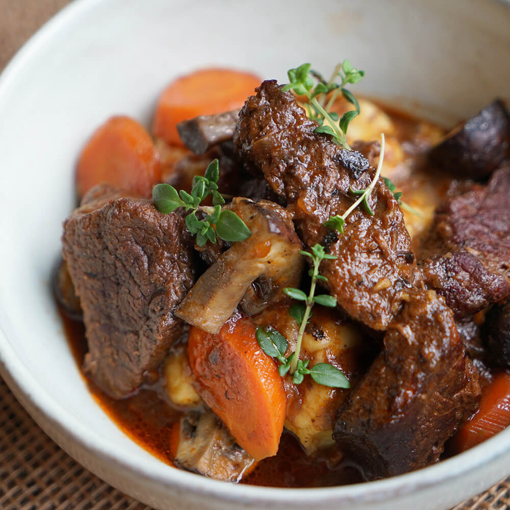 Rezept für Boeuf Bourguignon selbstgemachtes Boef Bourguignon mit frischen Karotten, Champignons, frischen Kräutern und einer dunklen Soße in einer weißen Schüssel serviert