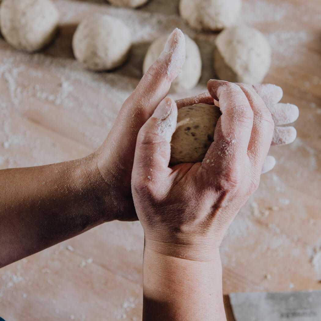 Jetzt in unseren Backkurs Profiwissen aneignen Zwei Hände formen einen Teigling