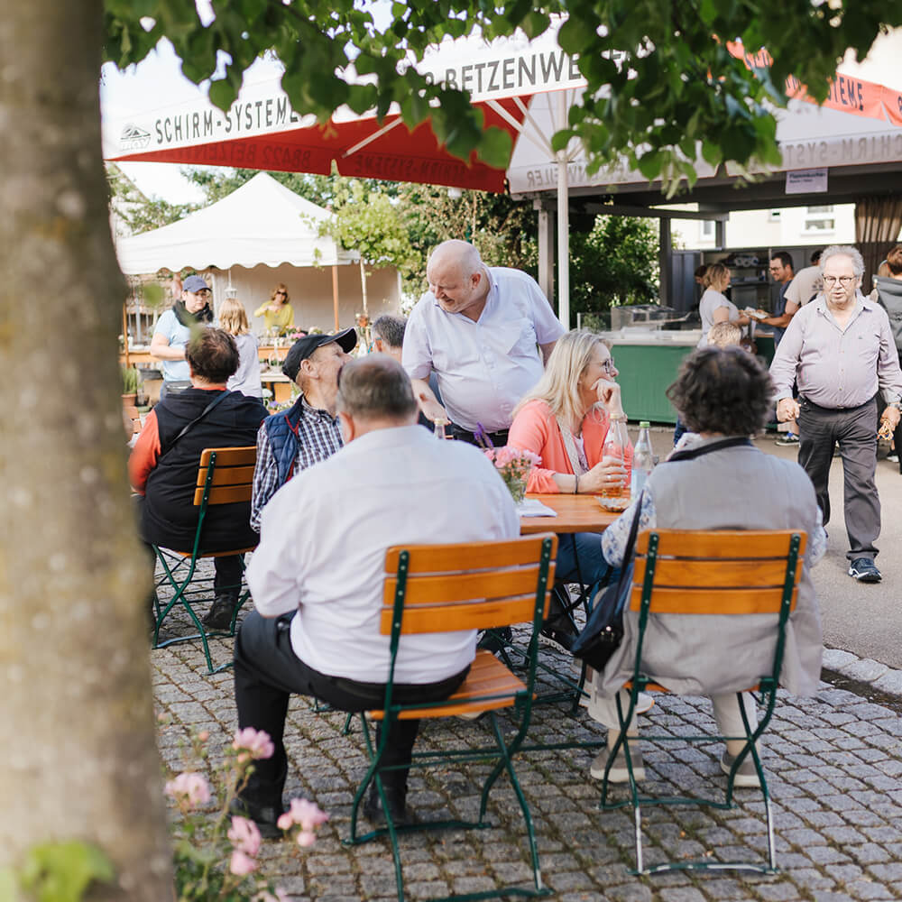 Häussler_Backtage Menschen sitzen gesellig an Tischen im Innenhof des Häussler Backdorfs bei den jährlichen Backtagen.