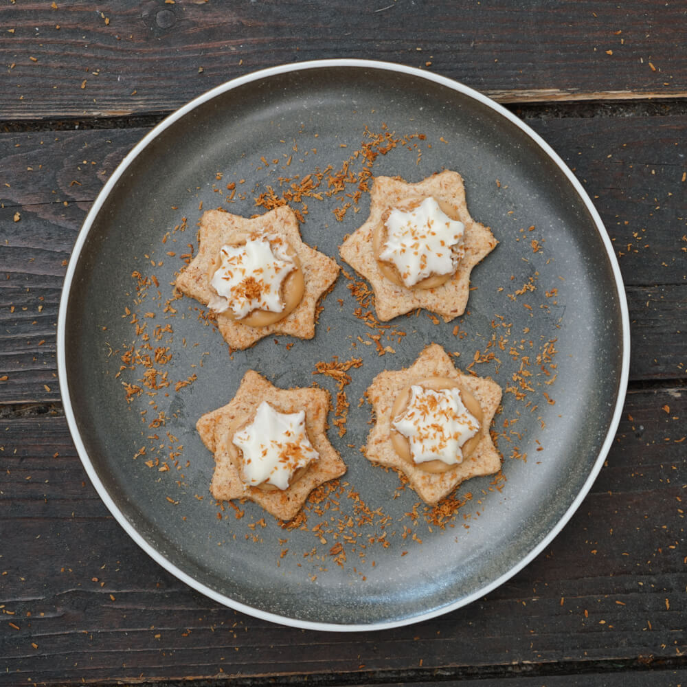 Rezept für Kokossterne mit Karamellfuellung aufeinder gesetzte Kokossterne mit Karamellfüllung auf einem grauen Teller serviert