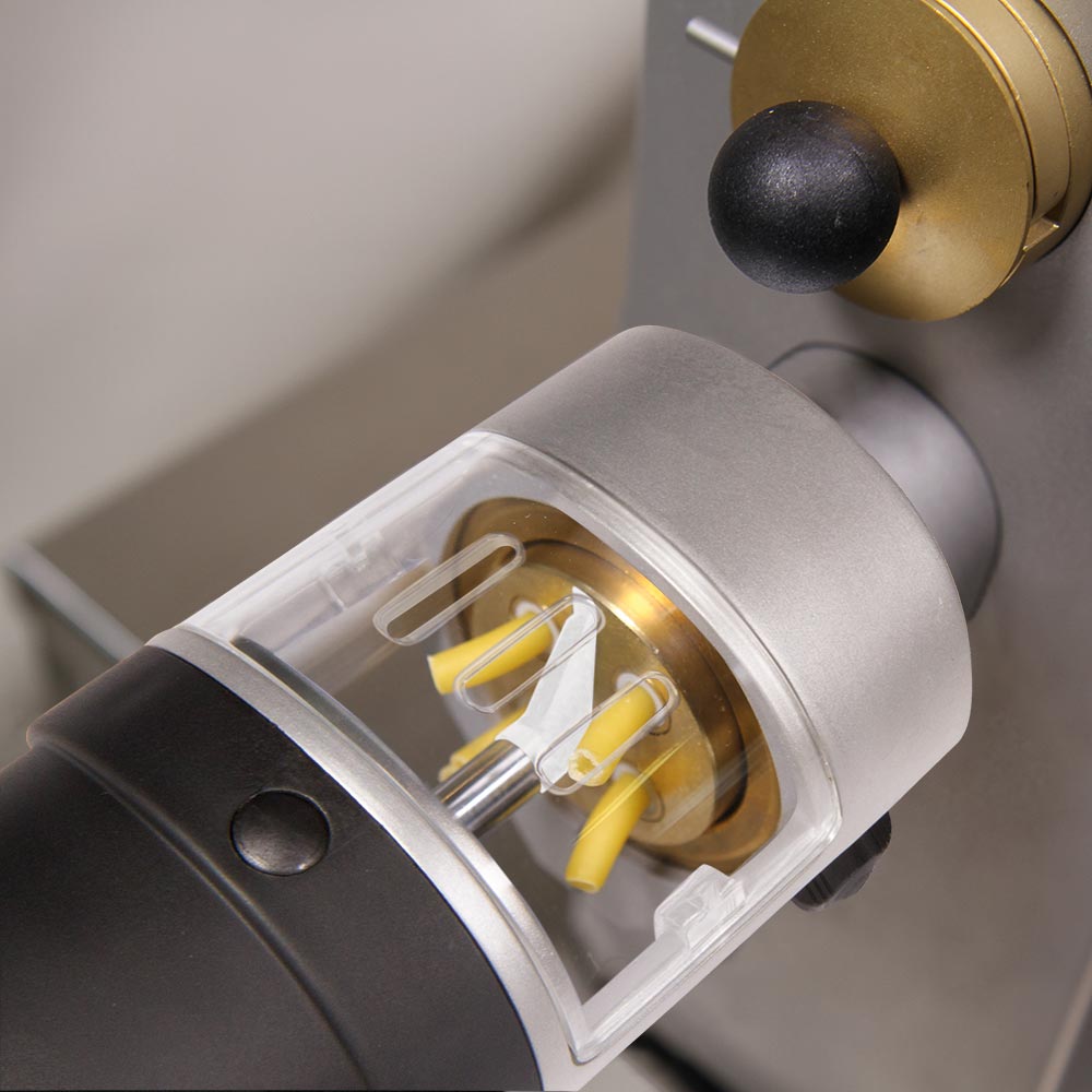 Auf dem Bild befindet sich ein Nudelschneider aus Edelstahl und schwarzem Kunstoff. Dieser Nudelschneider hat ob ein Sichtfenster aus Plastik. Der Nudelschneider ist an einer Nudelmaschine befestigt aus der Nudeln herauskommen.