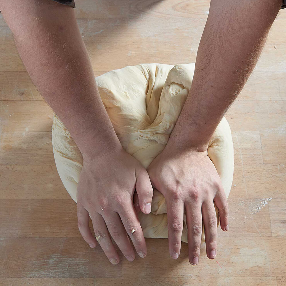 Teigknetmaschine SP10 Ein Teig wird mit der Hand auf einem Holzbrett bearbeitet