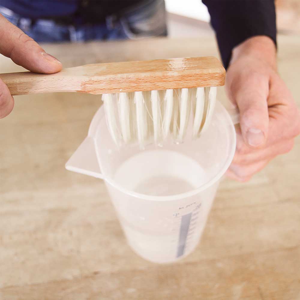 Ein Brotpinsel wird in einem Messbecher mit Wasser nass gemacht
