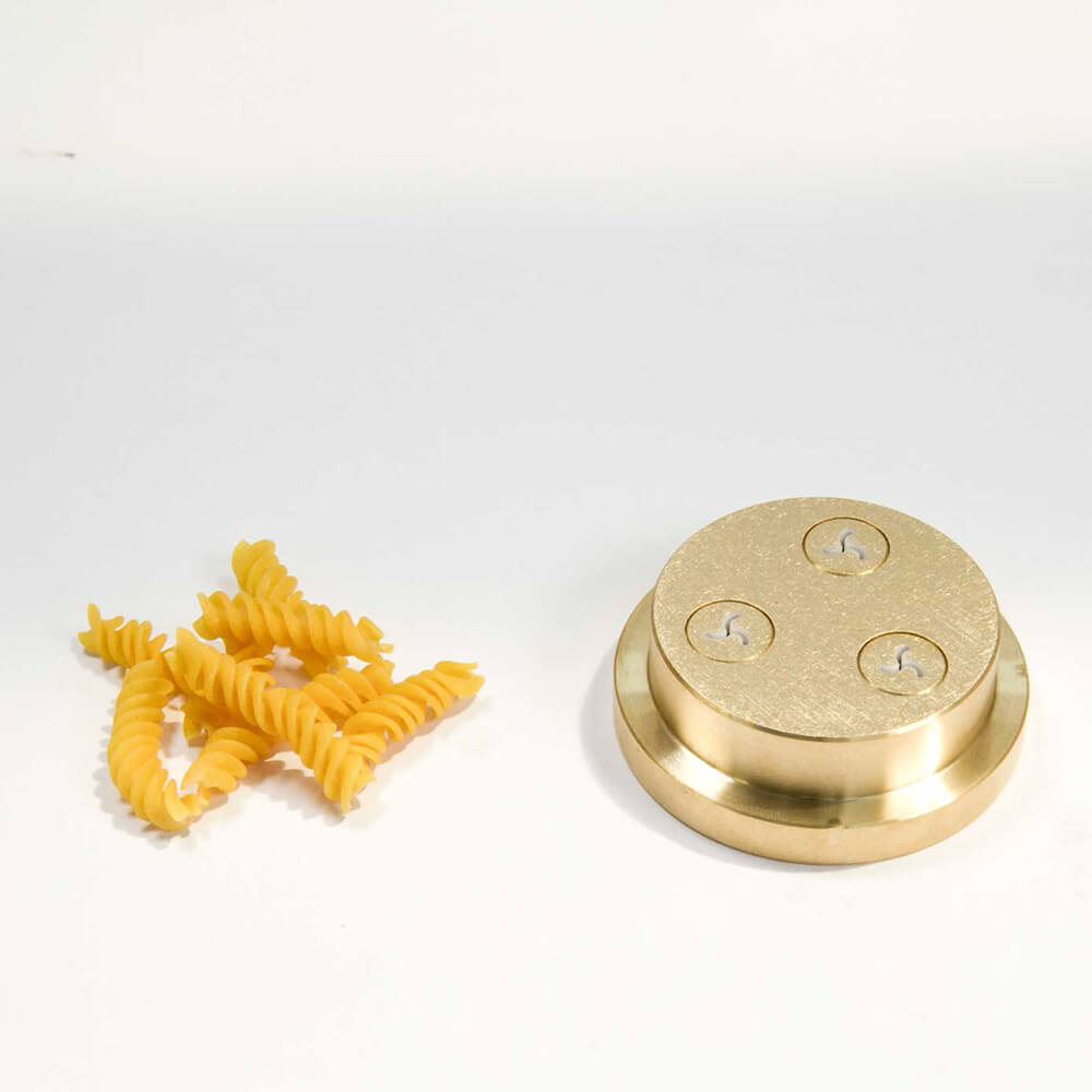 Nudelmatrize Nr. 49a für Fusilli neben einigen Fusilli-Nudeln vor einem weißen Hintergrund.