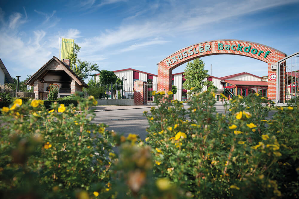 Aussenansicht_Backdorf Aussenansicht des Häussler Backdorfs mit dem großen Eingangstor, Holz- und Steinarchitektur und einladender Atmosphäre.