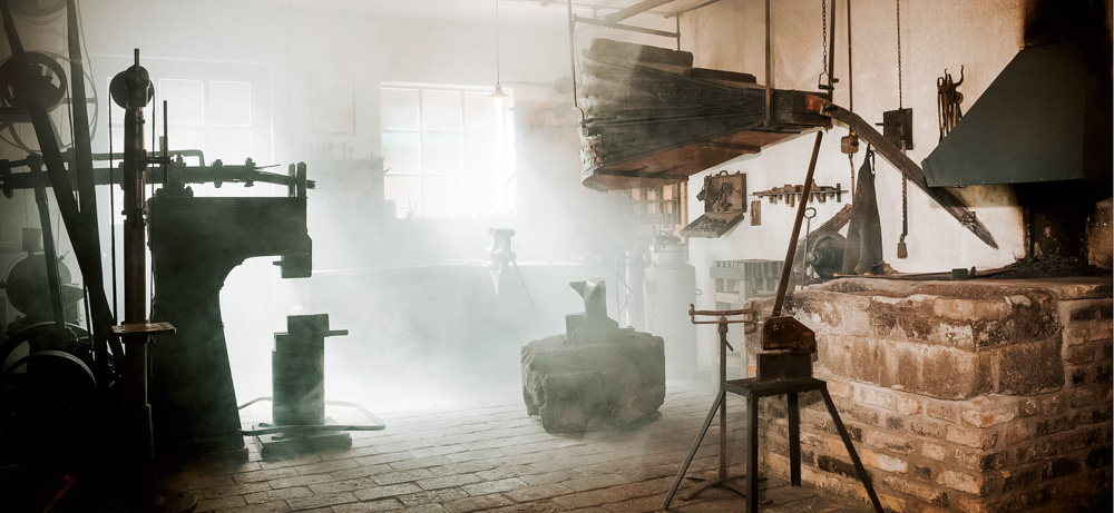 Historische Schmiede mit offener Feuerstelle, Amboss und traditionellen Schmiedewerkzeugen in rustikalem Innenraum