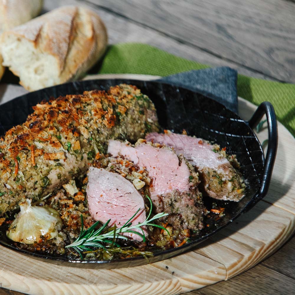 Schweinelende mit Kräuterkurste in einer Gusspfanne serviert mit einem Zwei Rosmarin und Baguette