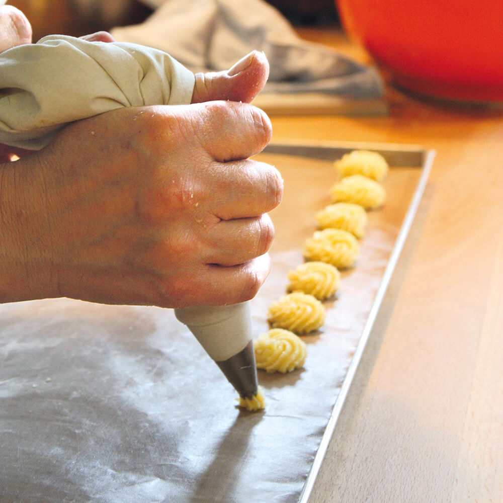 Spritzbeutelset in Benutzung, spritzt Rosetten auf ein Backblech
