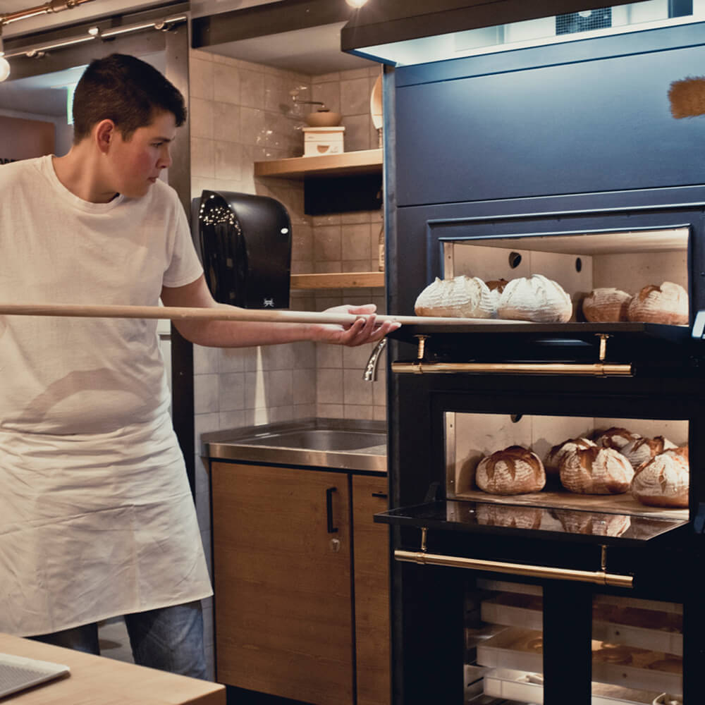 Brot backen im Häussler Elektro-Steinbackofen EIn junger Bäcker schießt Brote ein