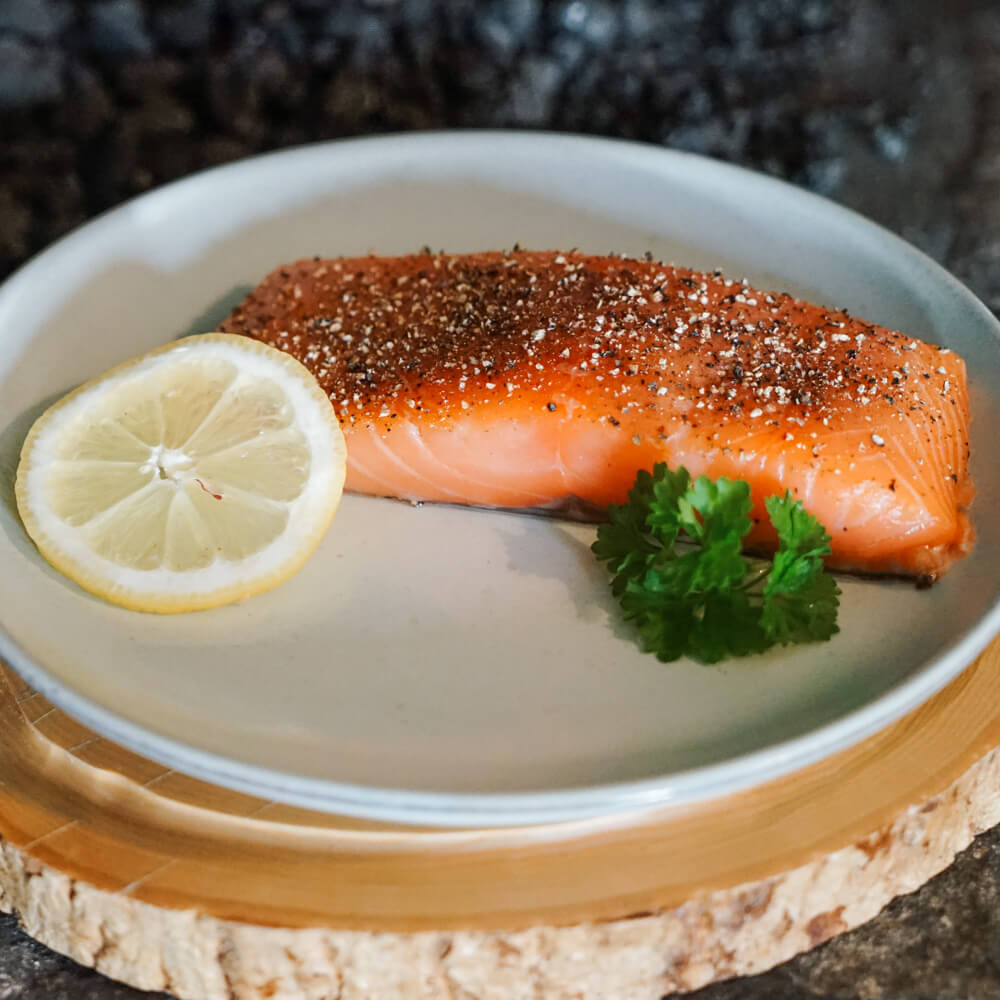 Rezept für Heißgeräucherter Lachs aus dem Holzbackofen geräucherter Lachs mit Pfeffer, einer Scheibe Zitrone und ein wenig Petersilie serviert auf einem weißen Teller
