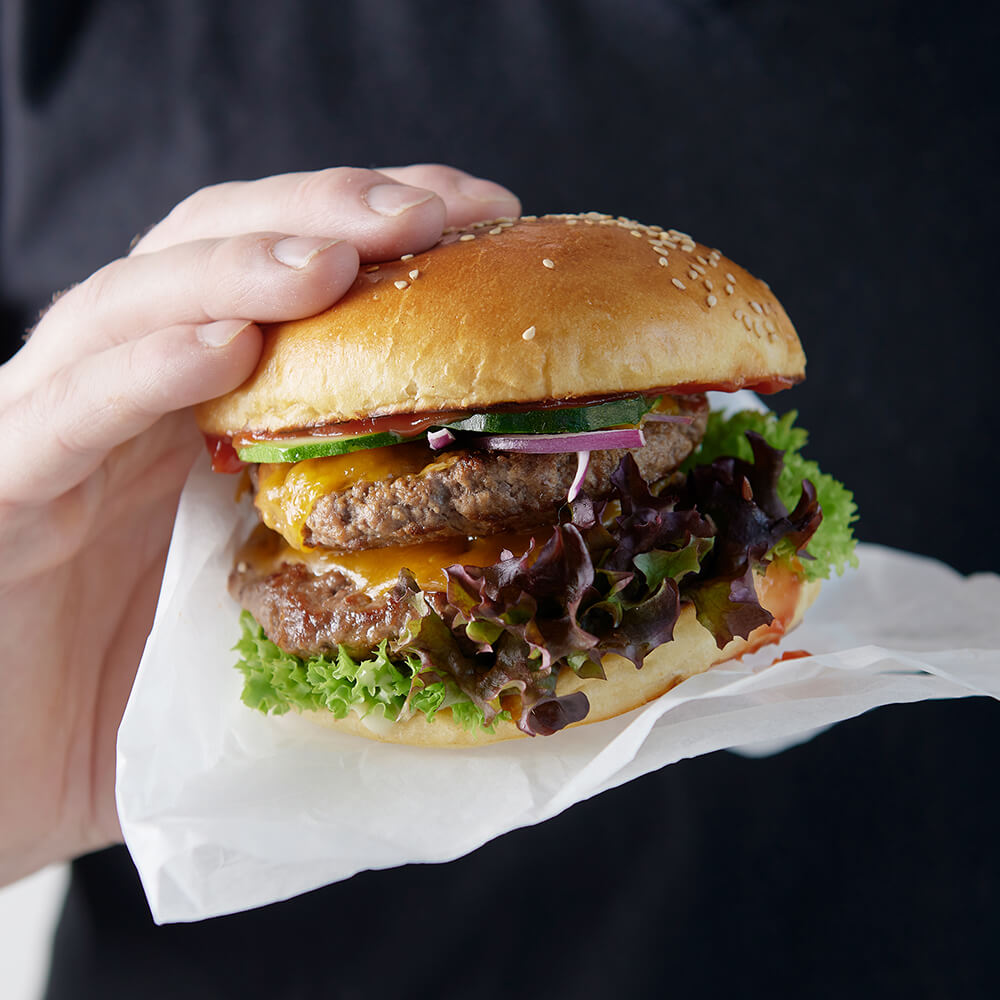 Burger_aus-Holzbackofen Frisch zubereiteter Burger mit saftigem Fleischpatty, knackigem Salat und Gurkenscheiben im goldbraunen Burgerbun.