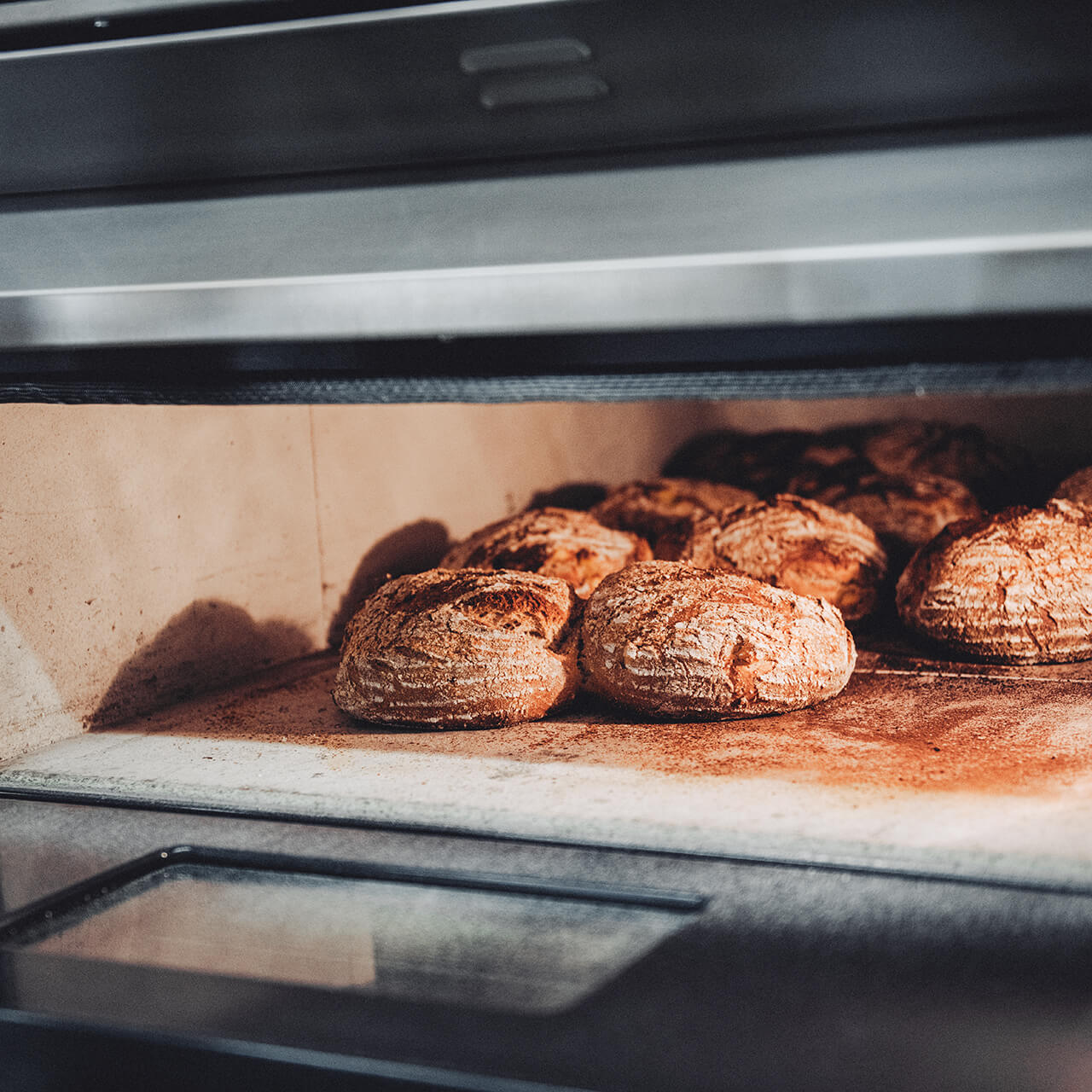 Elektro_Steinbackofen_mit_Broten Geöffneter Elektro-Steinbackofen in dessen Innenraum mehrere frisch gebackene Brote liegen.