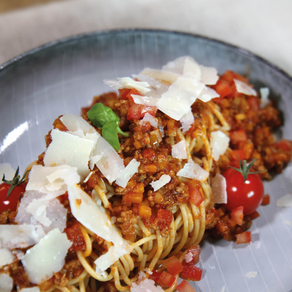 Rezept für vegetarische Bolognese selbstgemachte Nudeln mit vegetarischer Bolognese aus Pilzen, Gemüse und frischem Parmesan auf einem grauen Teller serviert