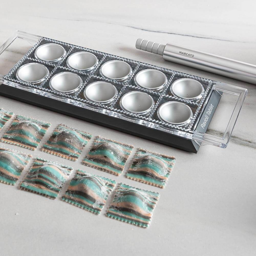 Raviolibrett Auf dem Bild befinden sich fertige Ravioli. Daneben liegt das Raviolibrett mit zwei Griffen sowie eine Teigrolle aus Edelstahl.