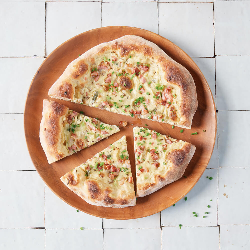 Rezept für Adelindes herzhafte Dinnete knusprige Dinnete mit Sauerrahm, Speck und Zwiebeln belegt auf einem Holzbrett serviert