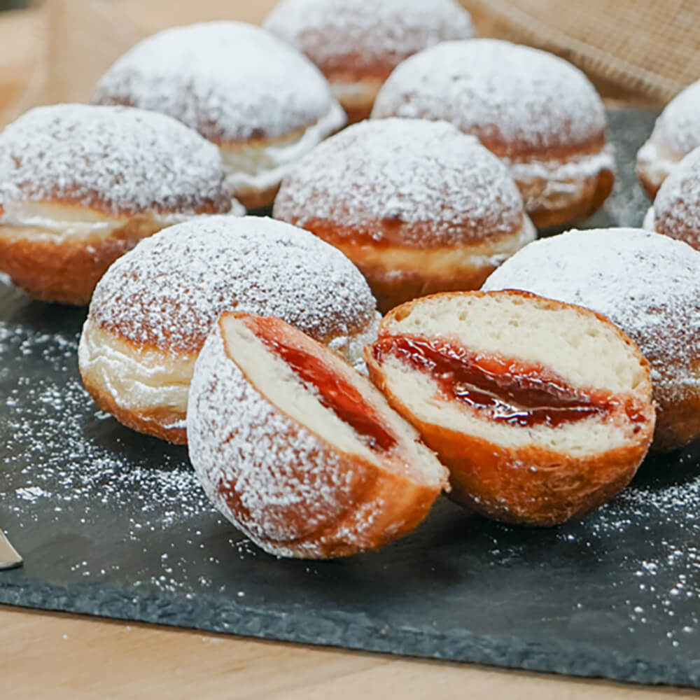 Mehrere gefüllte Berliner mit Puderzucker bestäubt auf einer Schieferplatte.