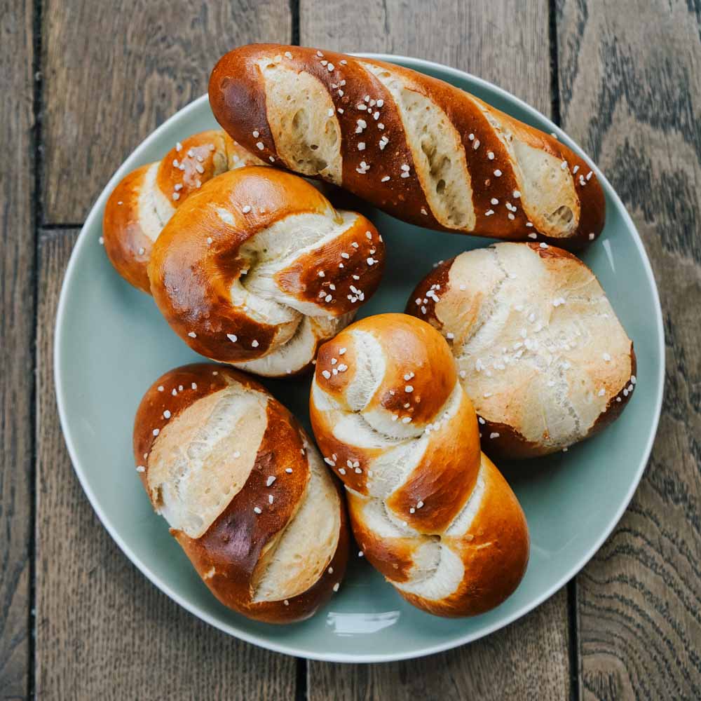 Rezept für Laugengebäck frische Laugenstangen und Zöpfe auf einem hellblauen Teller