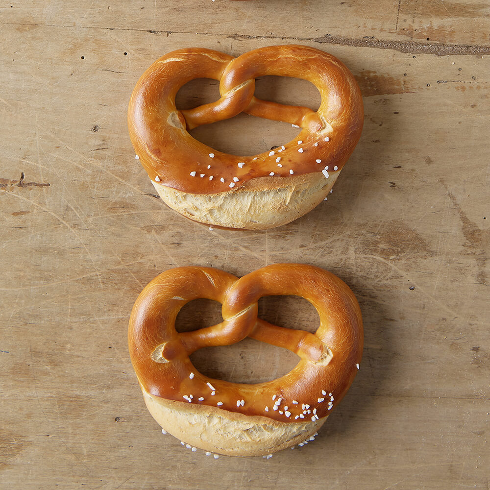 Rezept für Adelindes Brötchen und Brezeln 2 frische Brezeln mit grobem Brezelsalz auf einem Backbrett serviert