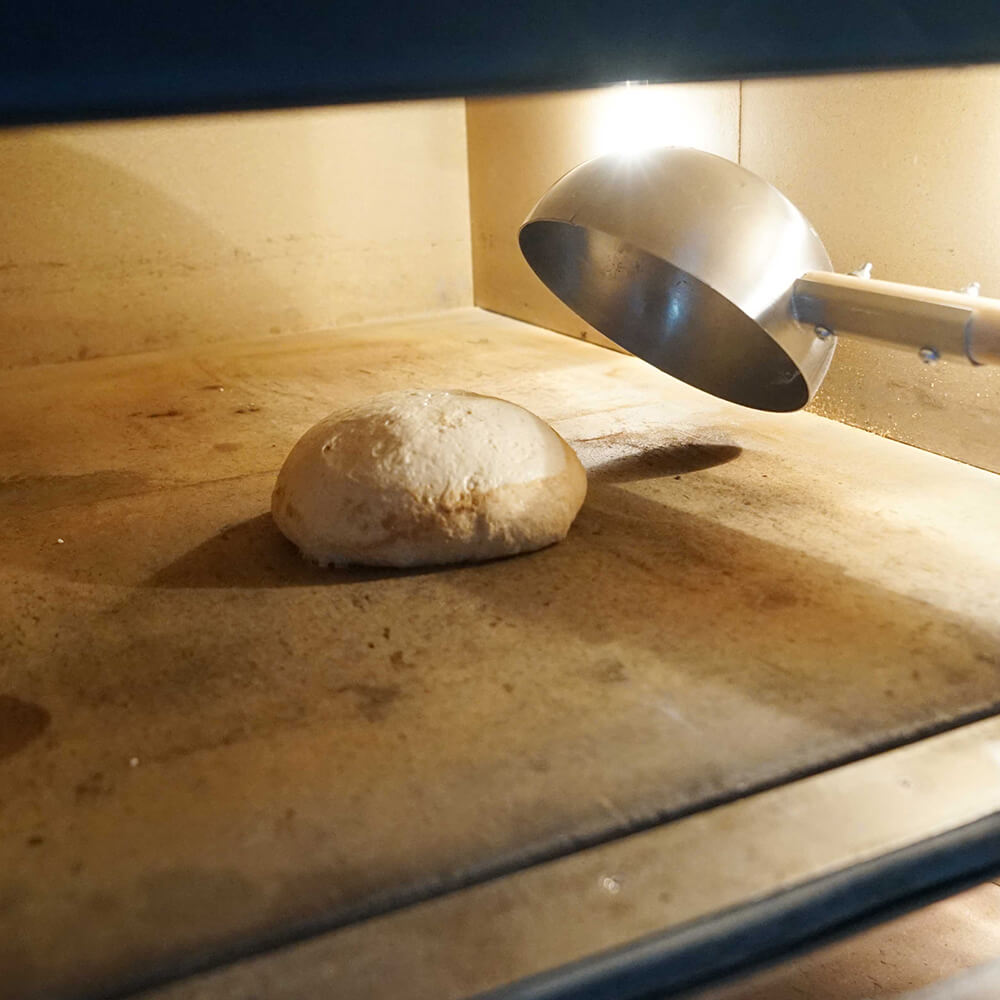 In einen geöffneten Ofen wird gerade ein Teigling mit einer Einnetzschüssel gelegt.