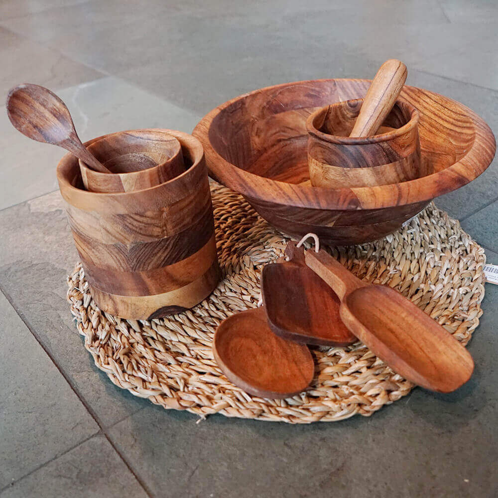 Schüssel, Töpfe, Kochlöffel aus Akazienholz auf einer geflochtenen Unterlage
