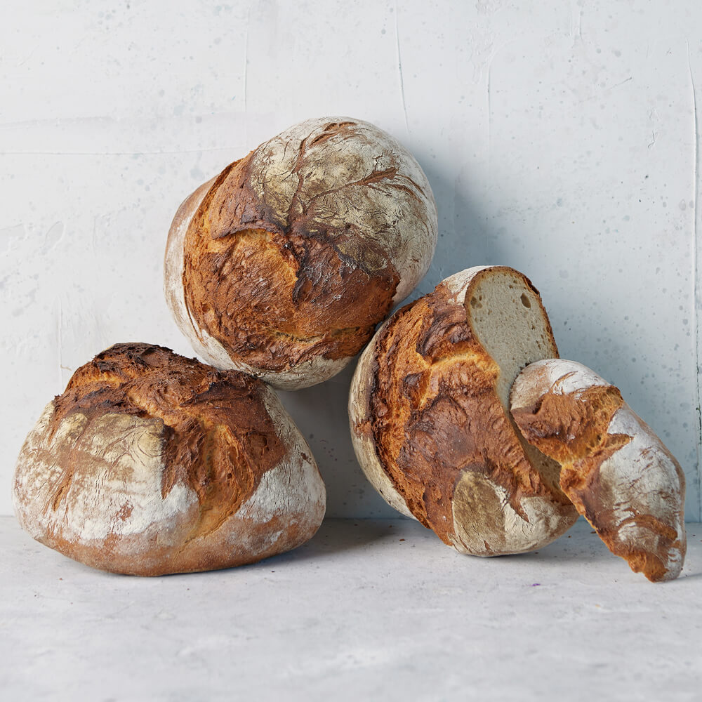 Rezept für Bauernbrot mit Mehlbrühstück Drei Bauernbrote aufeinander gestapelt auf grauem Hintergrund