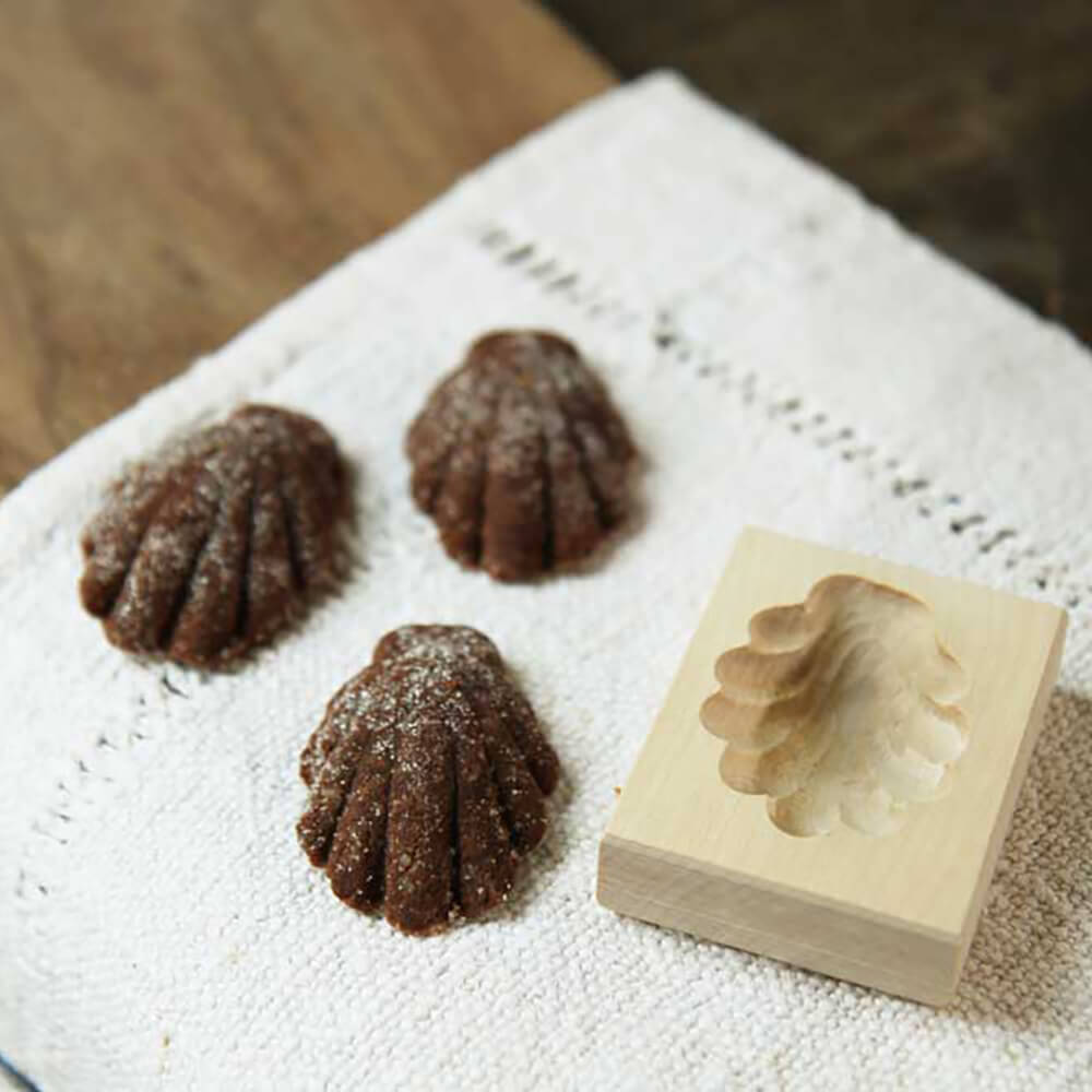 Bärentatzenform Bärentatzenform aus Holz. Links davon liegen 3 dunkelbraune Plätzchen. Diese liegen auf einem Leinentuch auf einer Holzarbeitsfläche