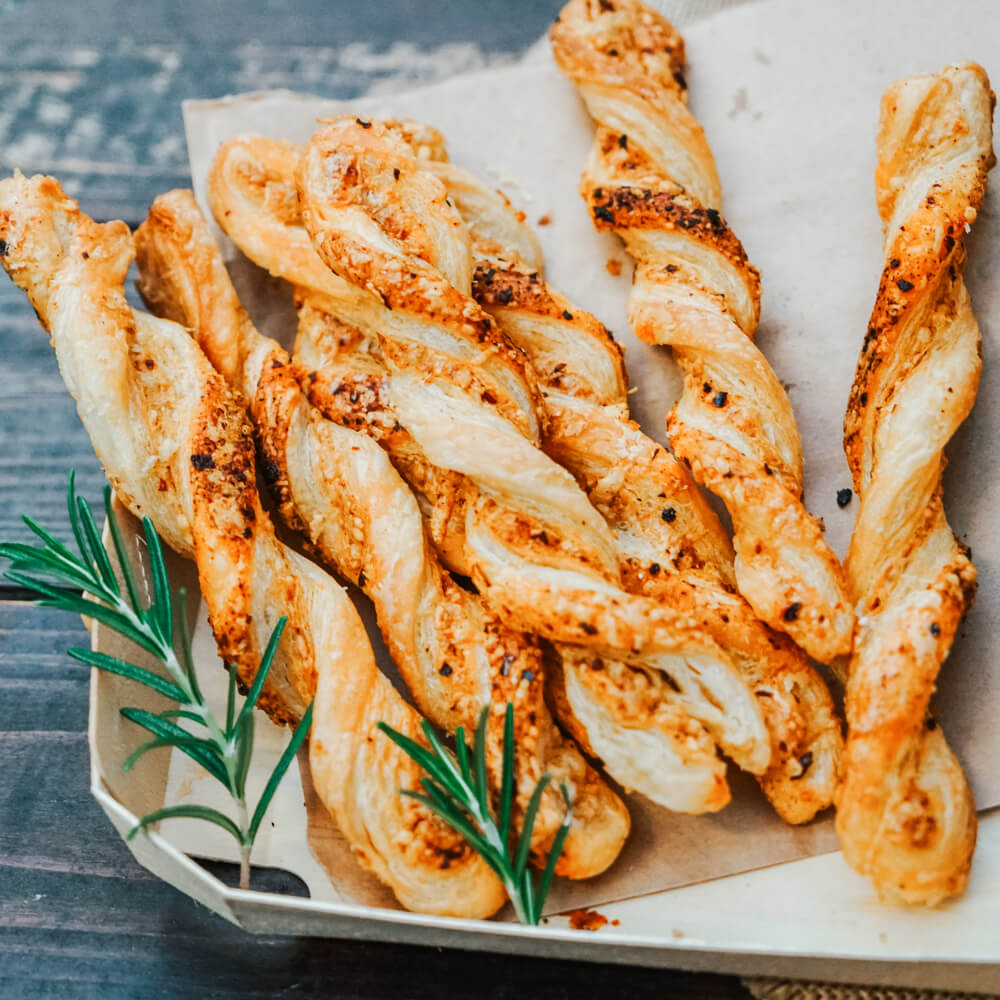 Rezept für Käsestangen aus Blätterteig knusprige Blätterteigstangen mit Käse auf einem weißen Teller mit zwei Zweigen Rosamarin serviert