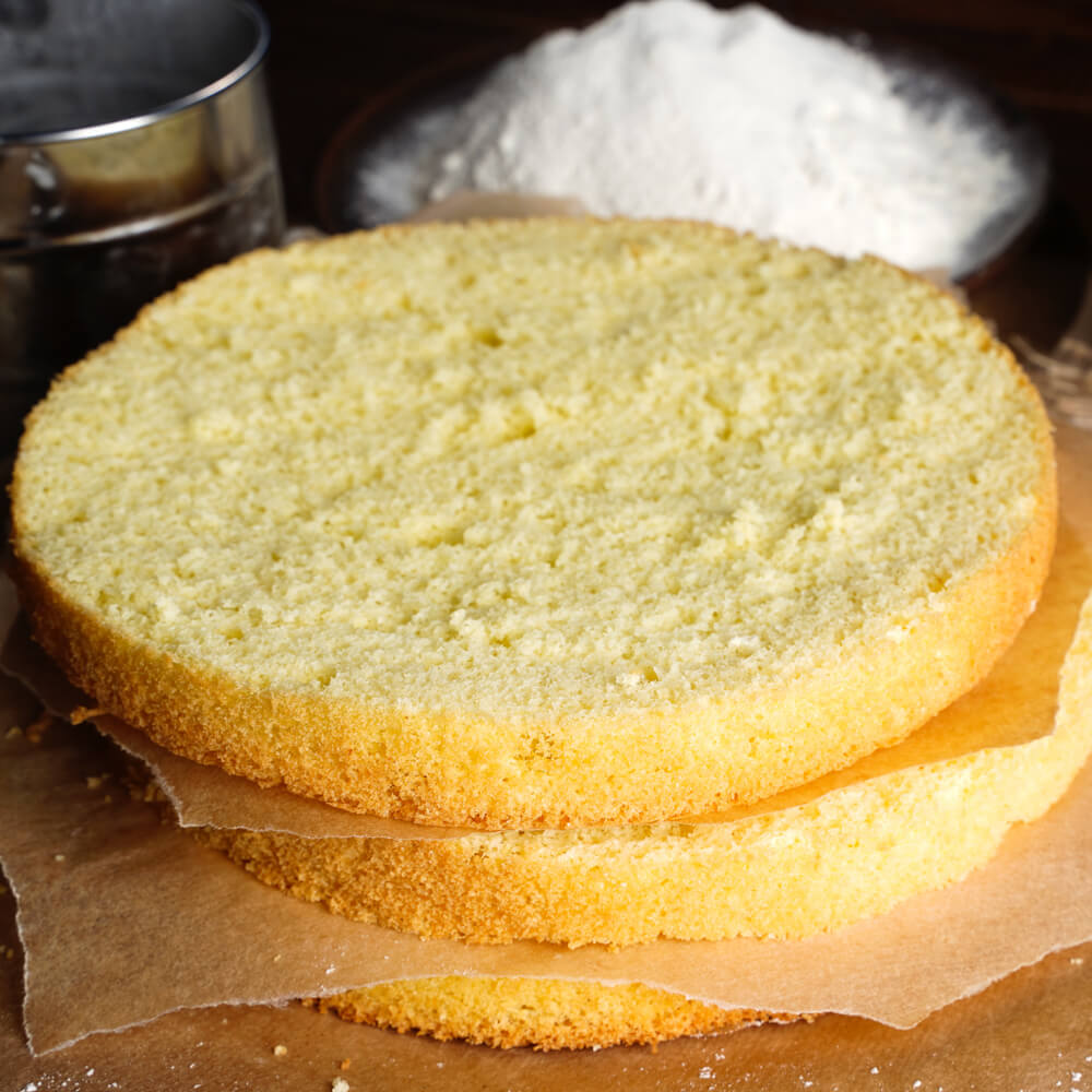 Drei Tortenböden auf einem Backbrett aufeinander gestapelt, mit ein Wenig im Hintergrund