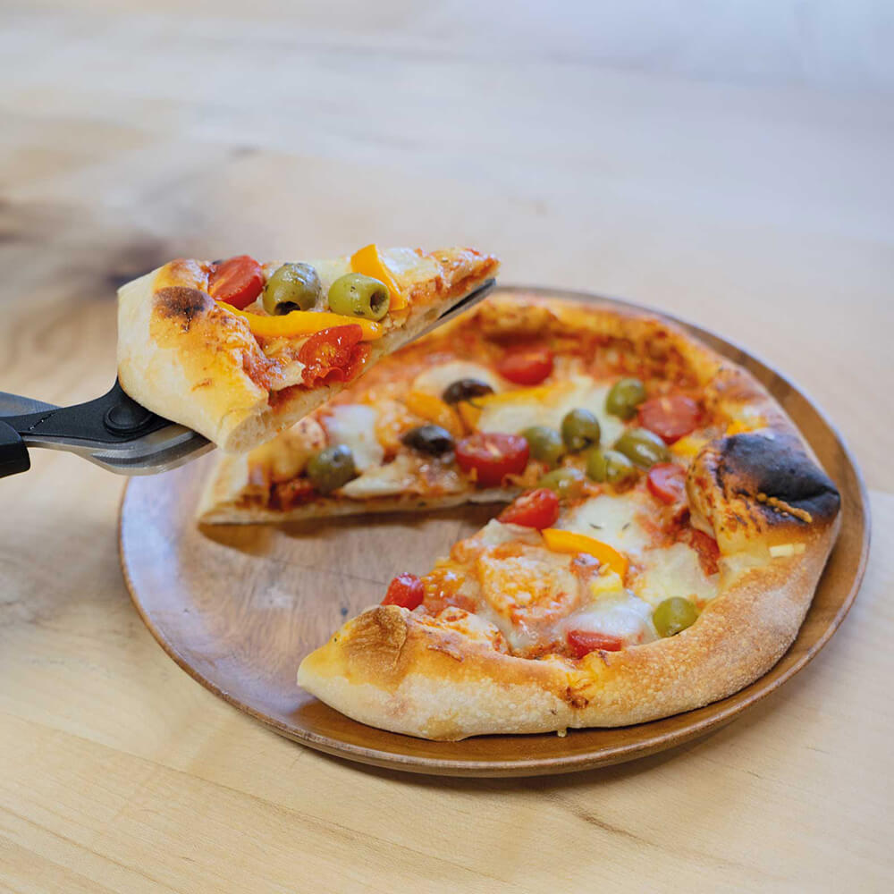 Eine Person hebt ein Stück Pizza, welches mit der Pizzaschere geschnitten wurde, mit der Pizzaschere wie eine Tortenschaufel an.