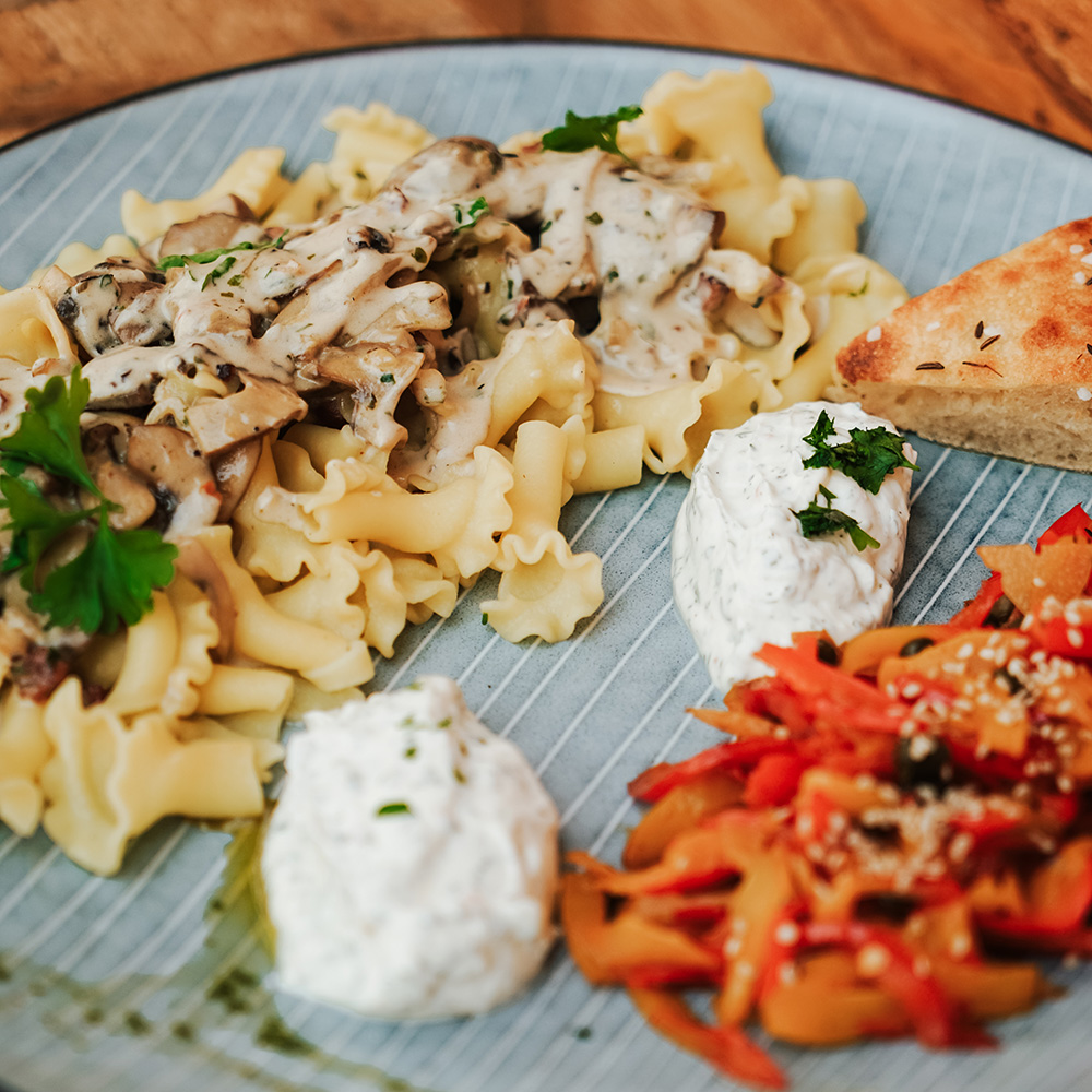 Rezept Knoblauchnudeln mit Peperonata und Champignon-Rahm-Sauce Knoblauchnudeln in Tulpenform mit Champignon-Rahm-Sauce darüber, serviert mit 2 Klecksen Kräuterdip und dazu Peperonata aus roter und orangener Paprika, Kapern und Sesamdrauf