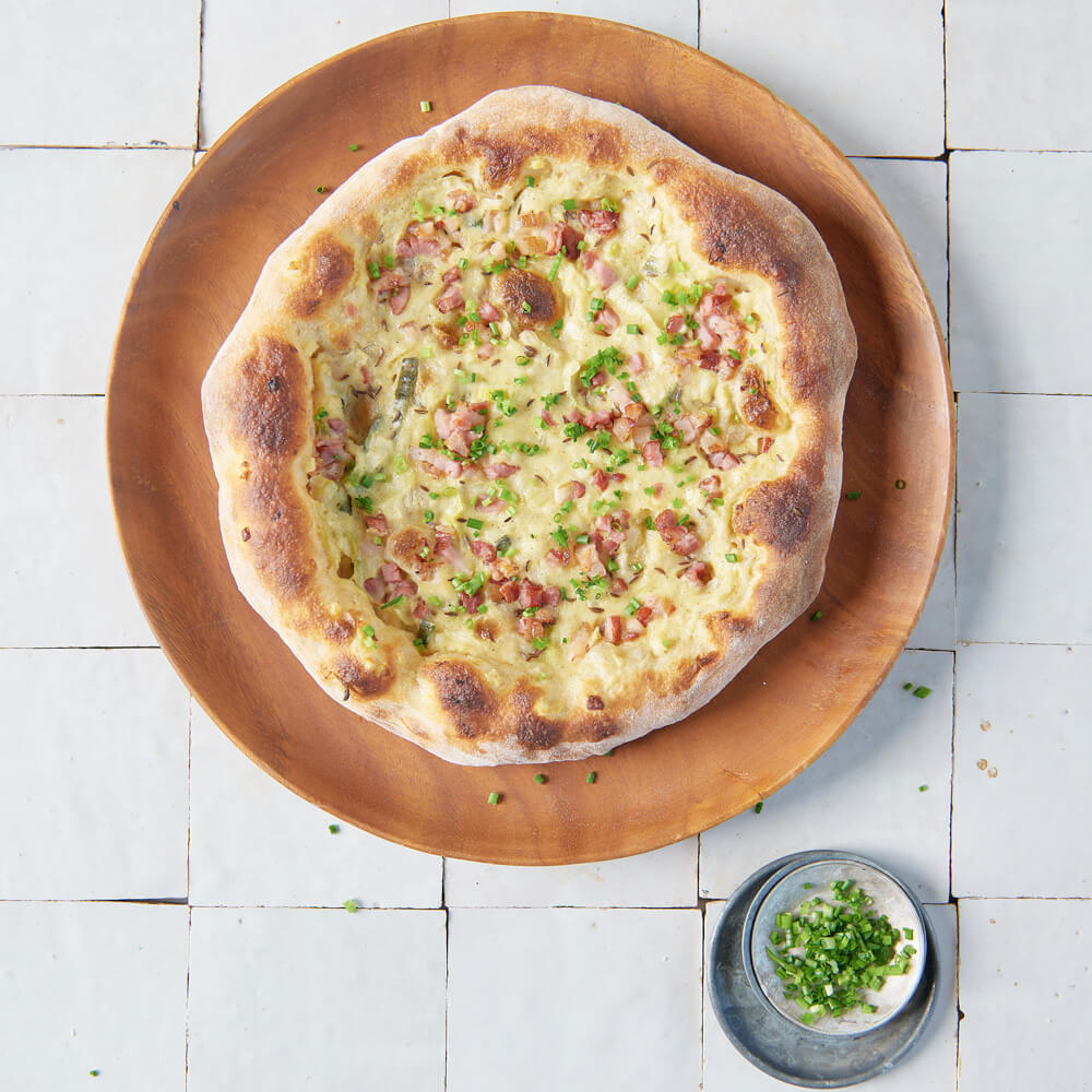 Rezept für Dinnete Herzhaft selbstgemachte Dinnete mit einem Belag aus Sauerrahm, Speck und Zwiebeln und mit Schnittlauch verfeinert. Auf dem Bild ist auch noch eine kleine graue Schüssel mit geschnittenem Schnittlauch