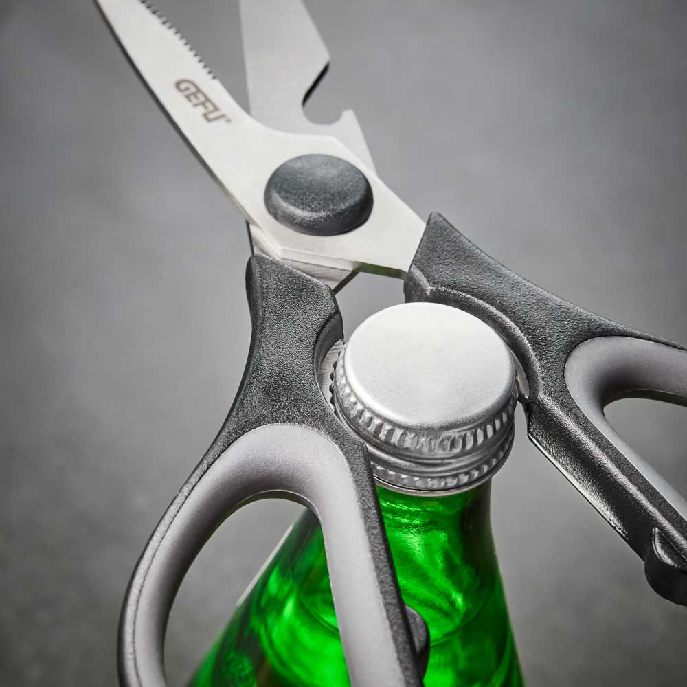 Die Schere umgreift den Deckel einer grünen Flasche auf einer Küchenarbeitsplatte.
