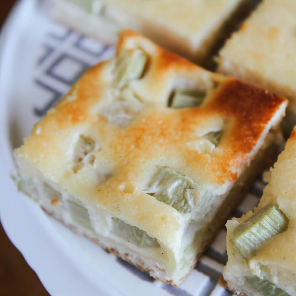 saftiger Rhabarberkuchen vom Blech mit einem Rahmguss auf einer Kuchenplatte serviert
