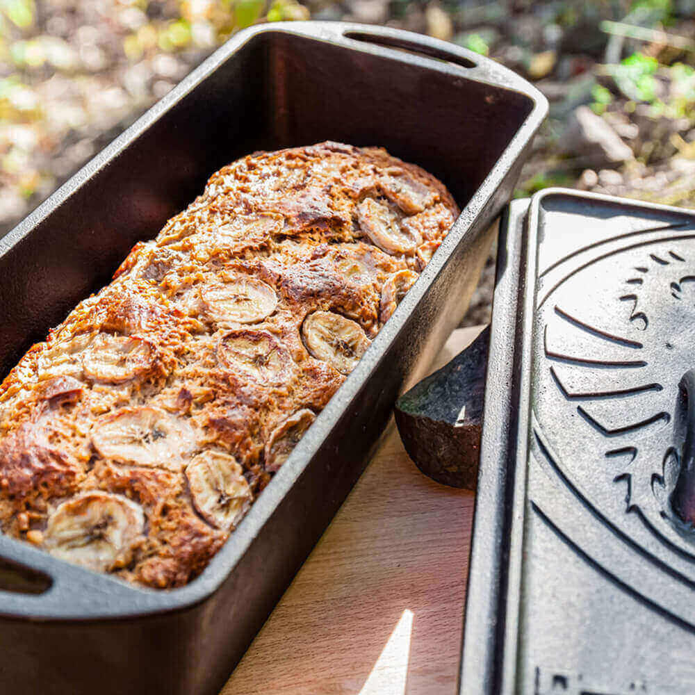 Gusseiserne Kastenform mit Deckel Offene Gusseiserne Kastenform mit frisch gebackenem Bananenbrot. Der Deckel liegt daneben