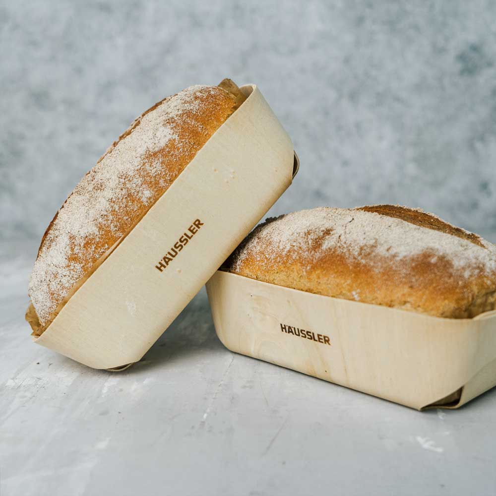 Kleines Mitbringsel mit Mehlmischung und Holzbrotform Goldbraun gebackenes Bauernbrot in der Holzbackform