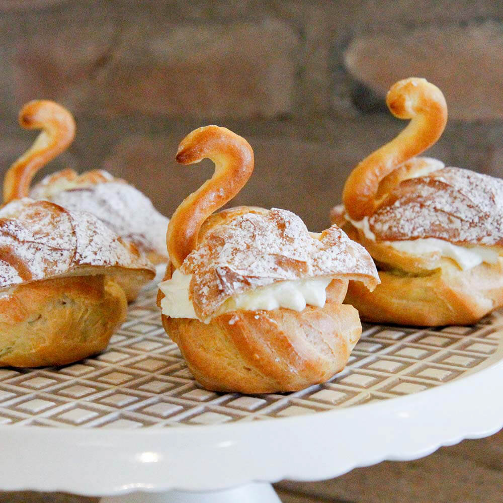 Rezept für Schwäne aus Windbeutel Windbeutel in Form von Schwänen mit einer Kirsch-Sahne-Füllung auf einer Tortenplatte serviert
