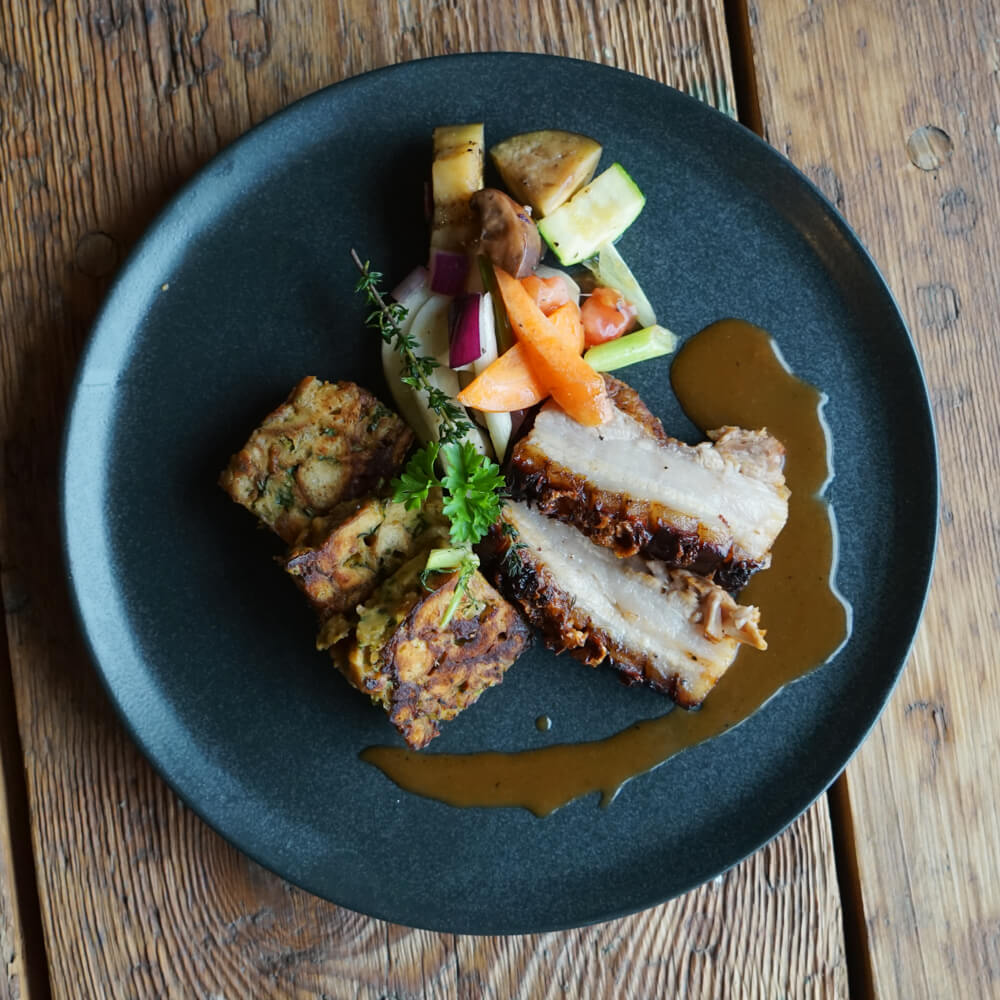 Rezept für Krustenbraten aus dem Holzbackofen Kurstenbraten mit Brezelknödel und firschem Gemüse auf einem schwarzen Teller serviert