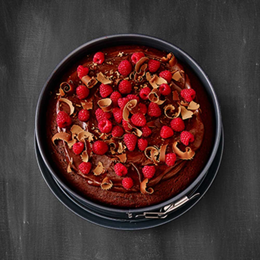 Springform Premium Baking Eine Kuchenform und ein Schokoladenkuchen mit Himbeeren und Schokoladenraspel steht auf einer Schwarzen Unterlage