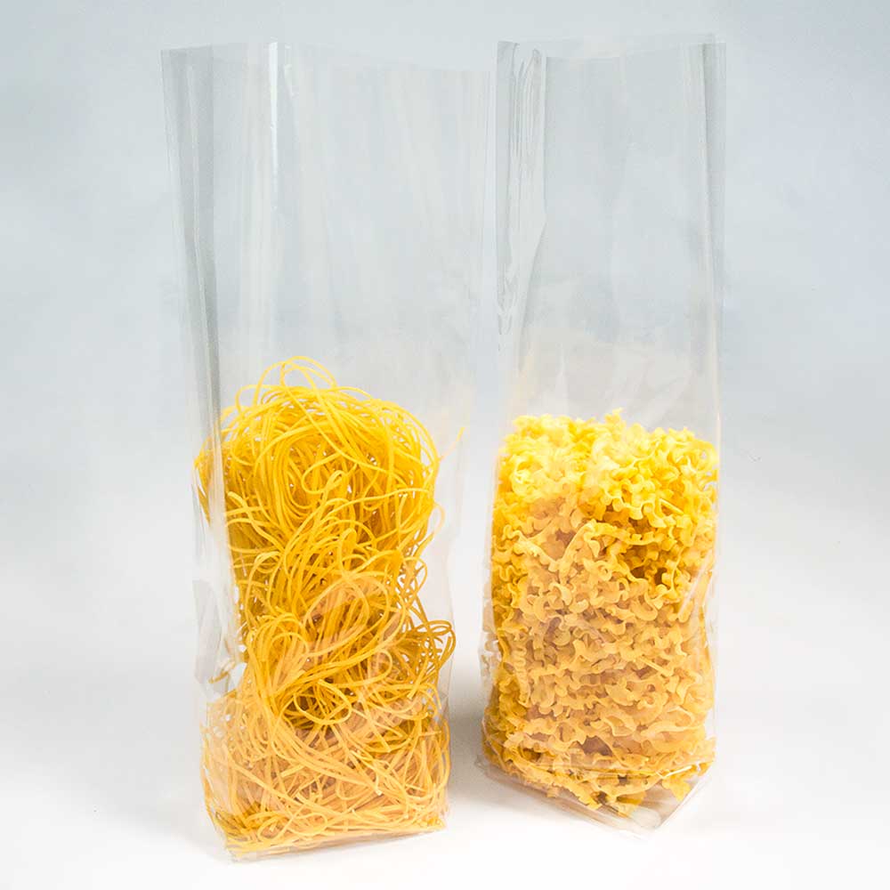 Zwei Nudel- und Plätzchenverpackungen aus transparenter Folie gefüllt mit zwei verschiedenen Nudelsorten vor einem weißen Hintergrund.