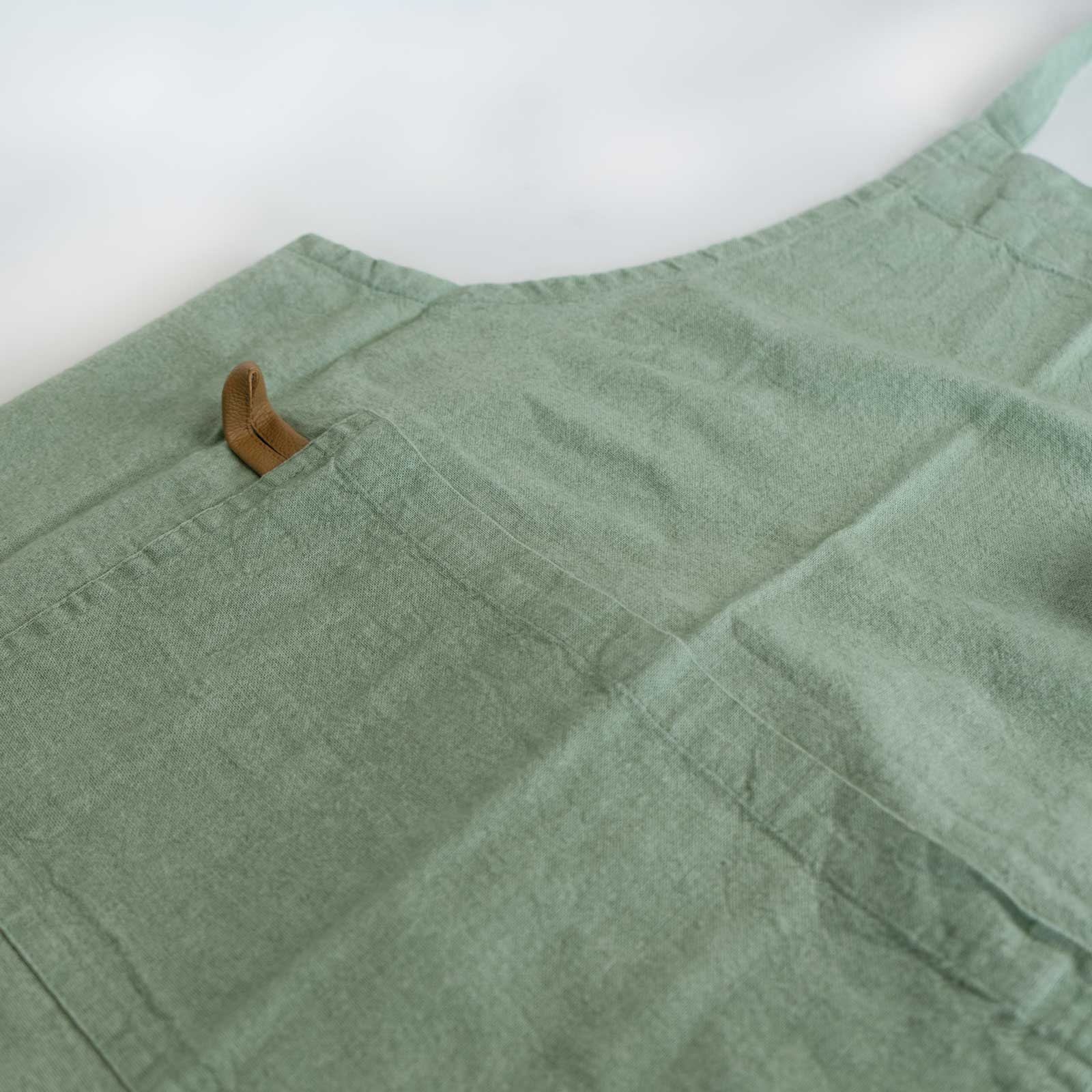 Schürze "MYRNA" grün Auf dem Bild befindet sich ein Ausschnitt einer grünen Schürze auf dem zu erkennen ist, das die schürze eine Tasche besitzt.