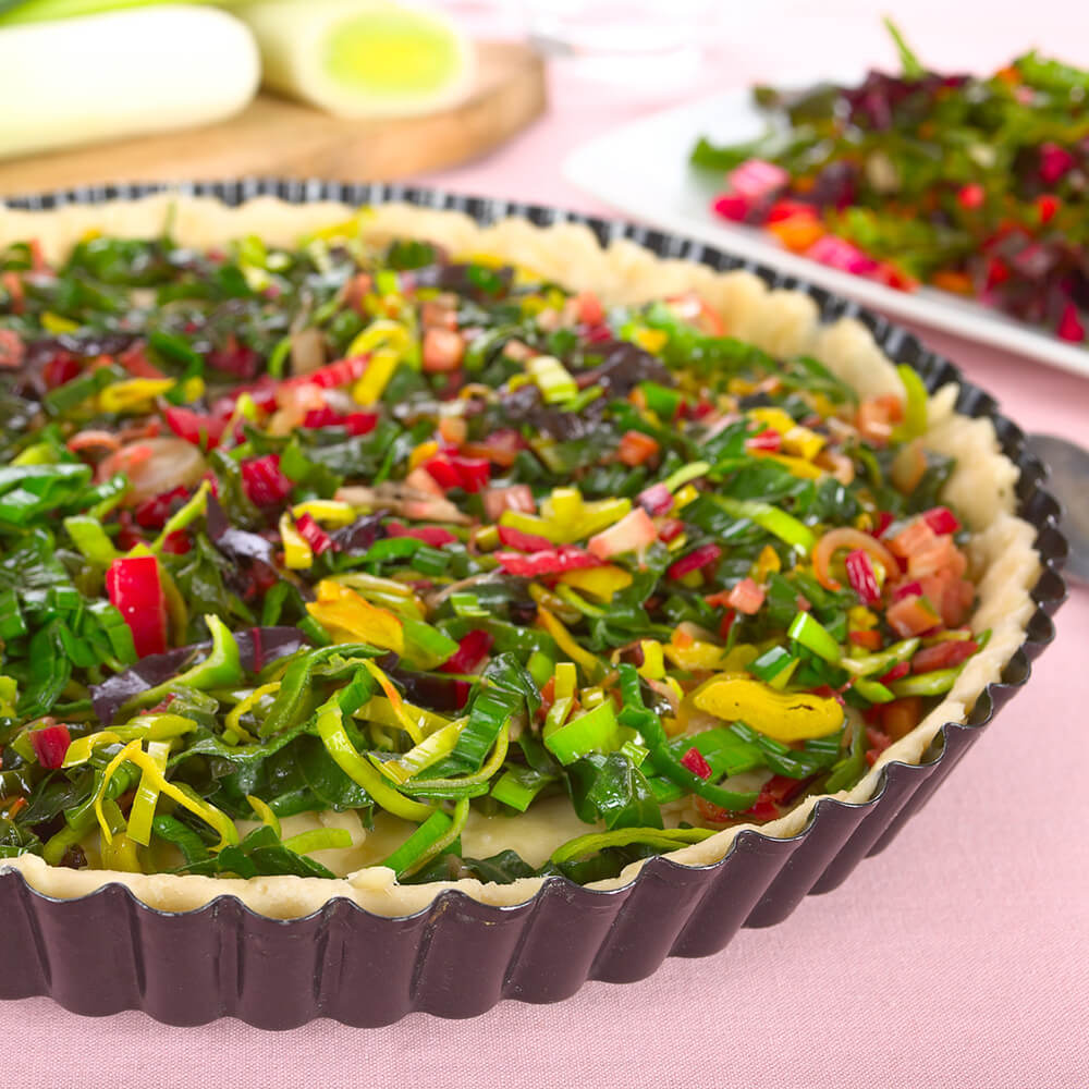 Quicheform mit einem Teig und geschnittenem Lauch, Tomaten und Paprika als Inhalt